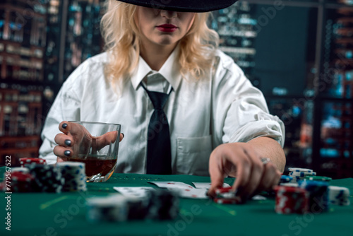 attractive girl in shirt and hat drinking whiskey and looking at poker cards in casino photo