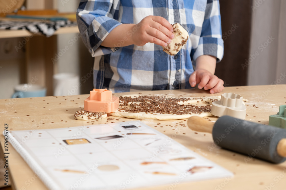 Child making his first cookie with a recipe book for toddlers, hands close-up