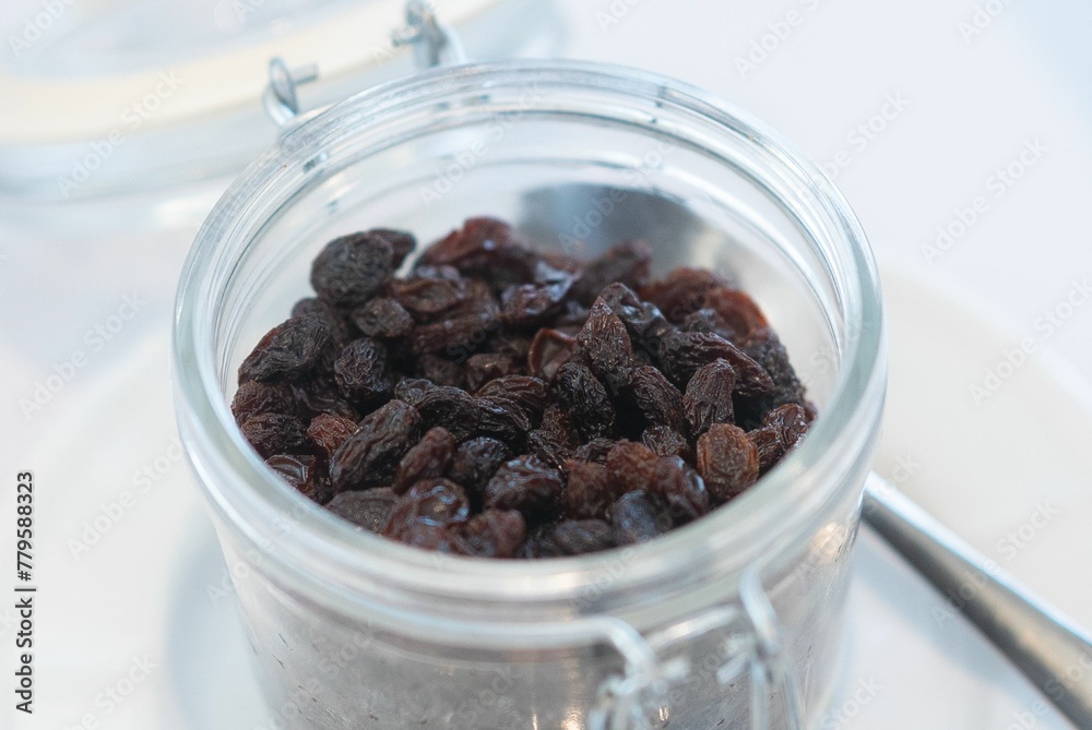 Closeup shot of sweet raisin in the glass jar put on the white table Closeup shot of sweet raisin in the glass jar put on the white table