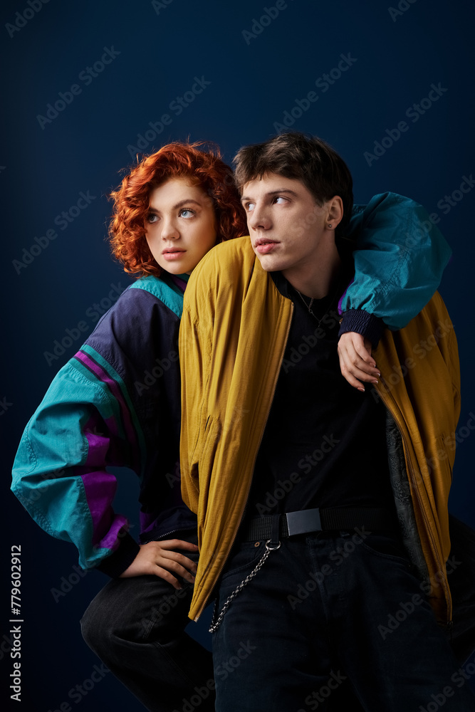 appealing stylish couple in fashionable vibrant attires hugging and looking away on blue backdrop
