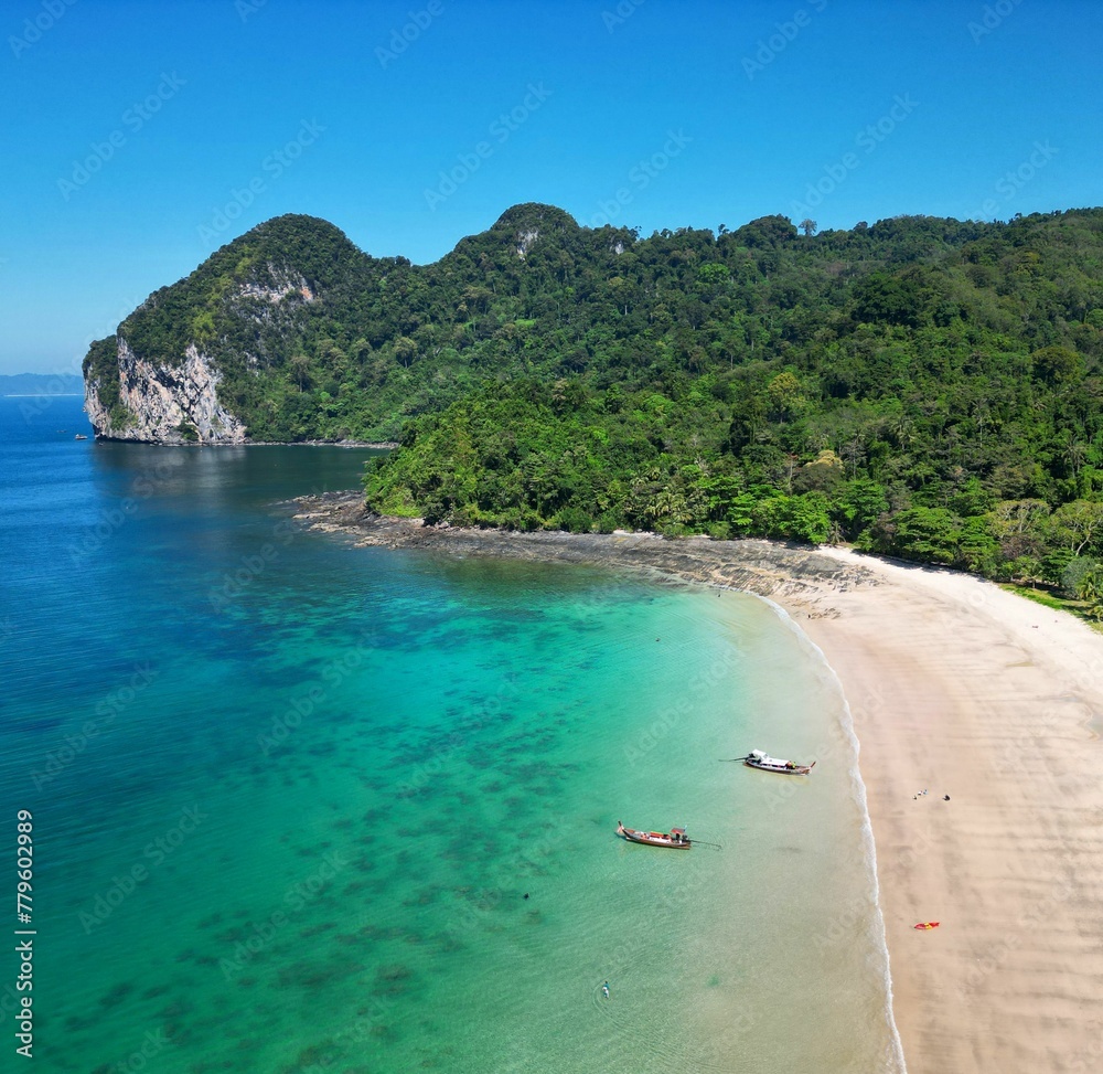 High-angle of Koh Mook Charlie beach resort with forested rocky cliffs on a sunny day