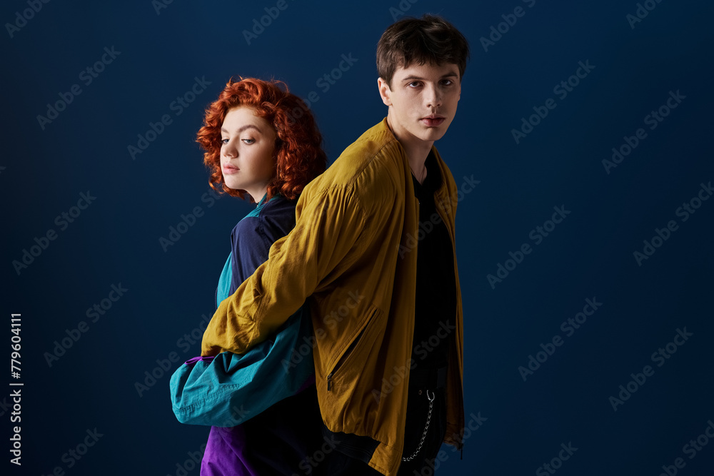 alluring woman posing back to back with her boyfriend who looking at camera on dark blue backdrop - obrazy, fototapety, plakaty 