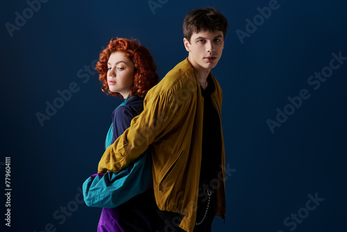 alluring woman posing back to back with her boyfriend who looking at camera on dark blue backdrop