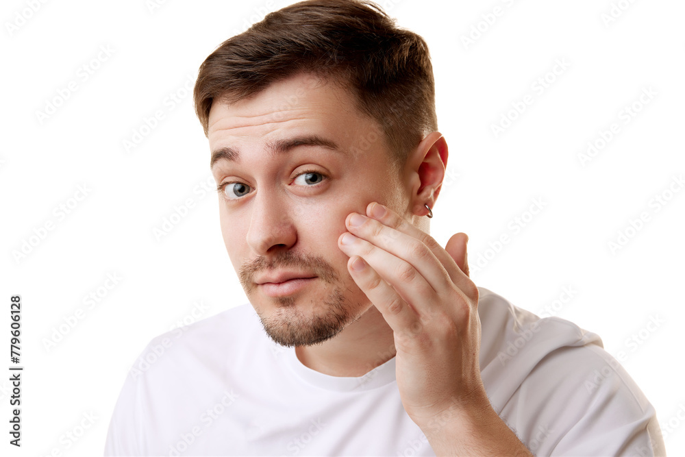 Young brunette man in T-shirt looking at camera and examine his skin after spa procedures against white studio background. Concept of natural beauty, male health, anti-aging, cosmetic products. Young brunette man in T-shirt looking at camera and examine his skin after spa procedures against white studio background. Concept of natural beauty, male health, anti-aging, cosmetic products.