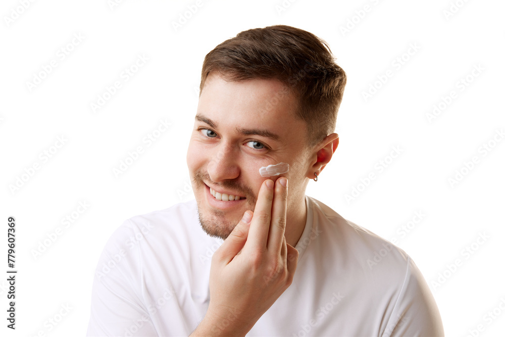 Young handsome man in T-shirt applying cream and looking with smile at camera against white studio background. Concept of natural beauty, male health, anti-aging, spa procedures, cosmetic products. Young handsome man in T-shirt applying cream and looking with smile at camera against white studio background. Concept of natural beauty, male health, anti-aging, spa procedures, cosmetic products.