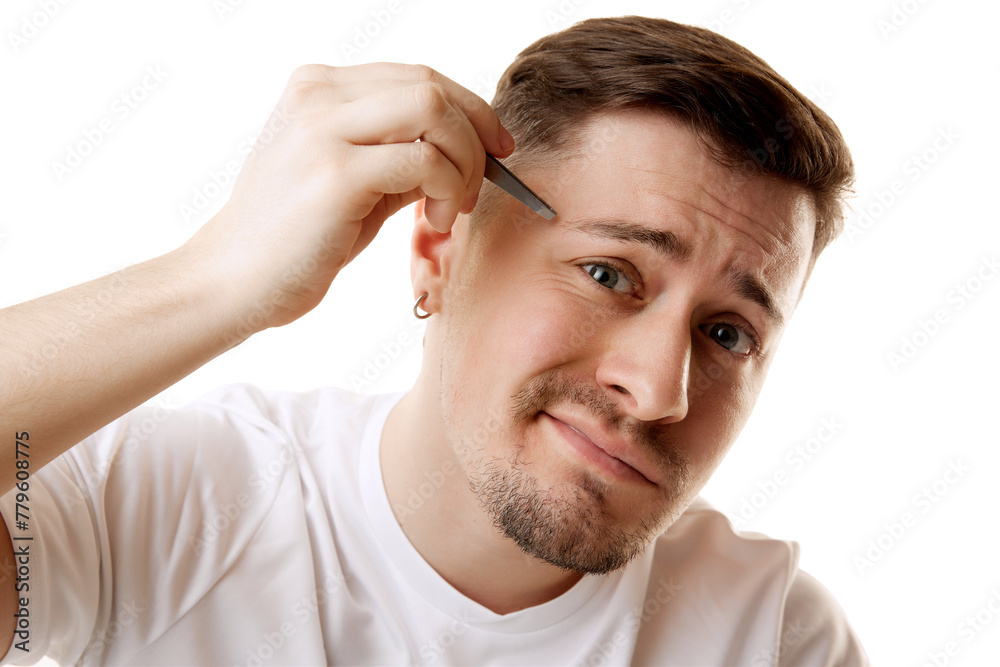 Young man in white T-shirt plucks his eyebrows with tweezers while looking at camera against white studio background. Concept of beauty, male health, anti-aging, spa procedures, cosmetic product Young man in white T-shirt plucks his eyebrows with tweezers while looking at camera against white studio background. Concept of beauty, male health, anti-aging, spa procedures, cosmetic product