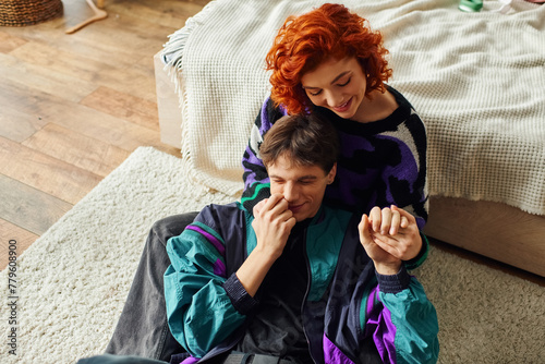 passionate red haired woman in cozy attire smiling and hugging her loving handsome boyfriend