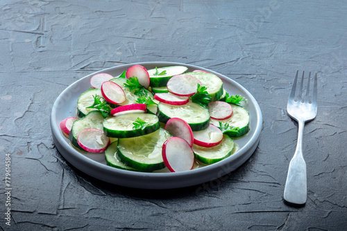 Fresh cucumber and radish salad with parsley, with a fork. Simple vegan recipe on a stone background. Healthy diet