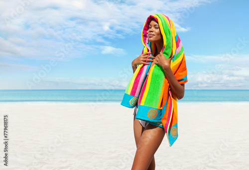 Woman at the beach side wrapped in a colorful towel, African latin American woman enjoying a sunny day with blue sky. Concept of summer beach holiday or booking travel and resort accommodations