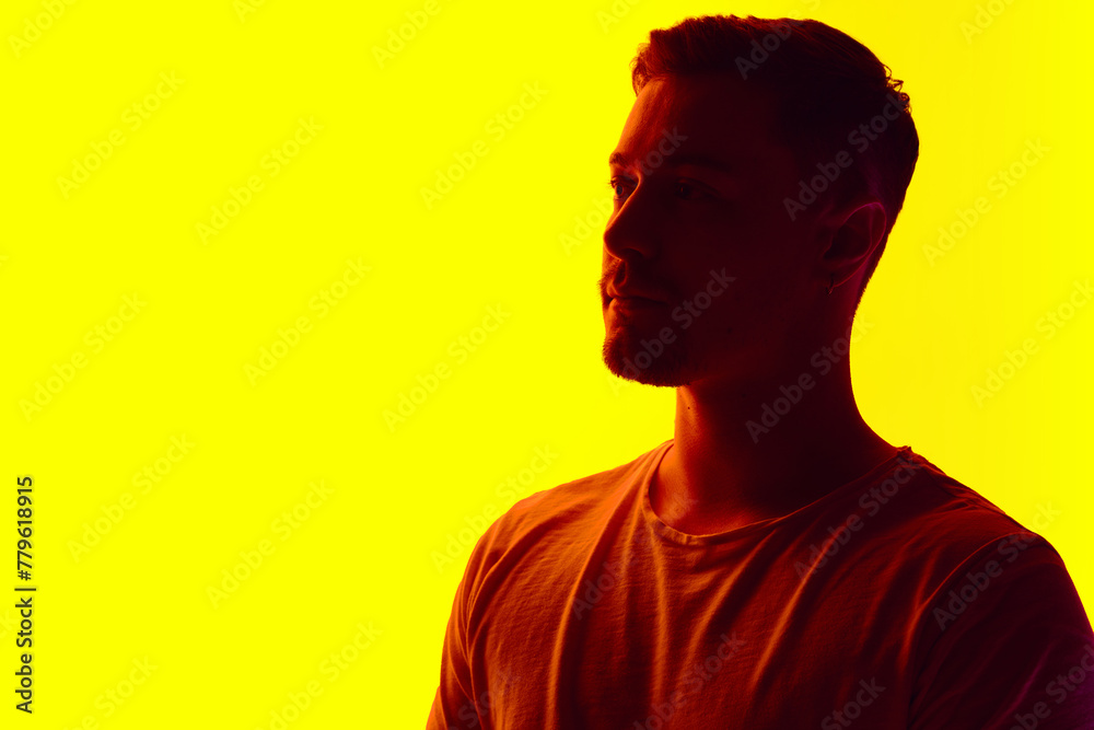 Silhouetted man in T-shirt posing in red neon light against vibrant yellow studio background. Concept of natural beauty, male health, anti-aging, spa procedures, cosmetic products. Silhouetted man in T-shirt posing in red neon light against vibrant yellow studio background. Concept of natural beauty, male health, anti-aging, spa procedures, cosmetic products.