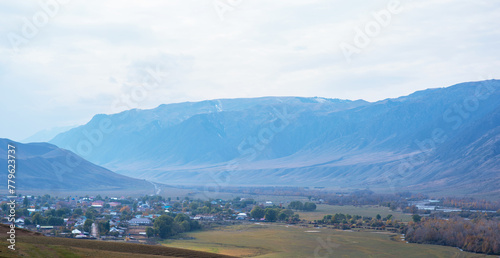 Small town in rural valley between mountains. Scenic view on a village with river, fields and gardens In mountain valley.