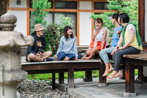 Group of five Japanese friends casually enjoying a conversation on a traditional Japanese porch, surrounded by lush greenery and a serene ambiance photo