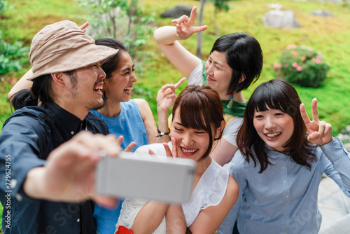 A group of five cheerful Japanese friends taking a selfie together outdoors, with a man holding the phone and everyone smiling broadly photo