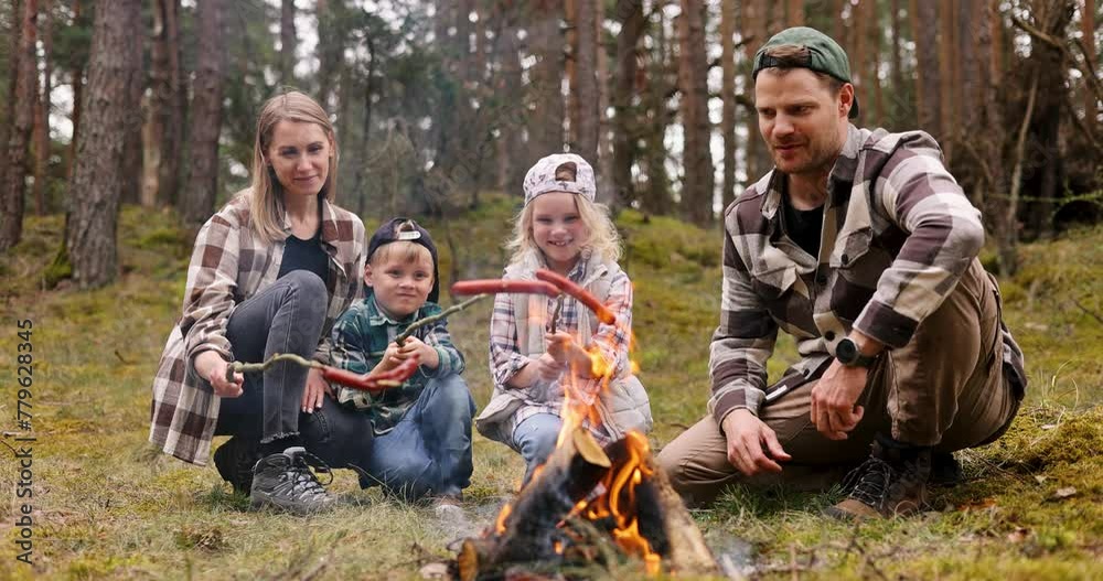 family with kids cook sausages on wooden skewers over a campfire in the forest. nature picnic, outdoor activities family with kids cook sausages on wooden skewers over a campfire in the forest. nature picnic, outdoor activities