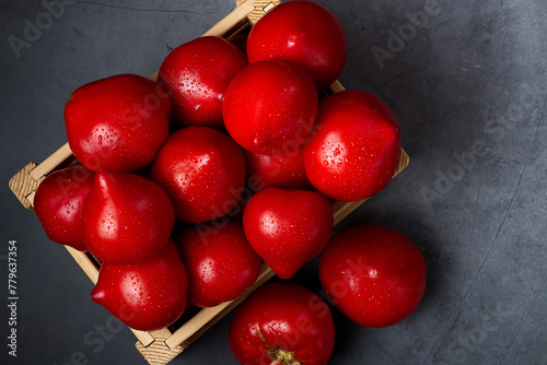 Top view of heap red, fresh, aromatic, ripe tomatoes with water drops in a wooden box against dark blue background