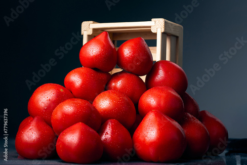 Heap of red, fresh, aromatic, ripe tomatoes with water drops near a wooden box