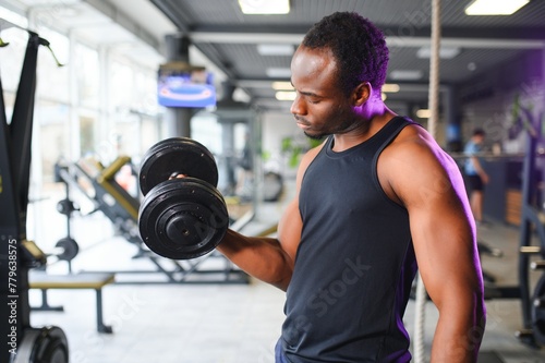 Young man strengthening biceps with dumbbell in gym