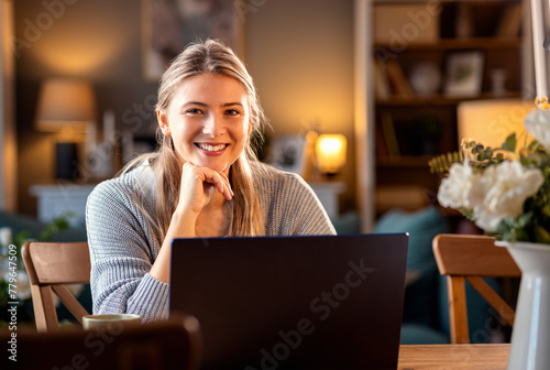 Smiling young woman working at home using laptop while sitting in her living room. © Zoran Zeremski