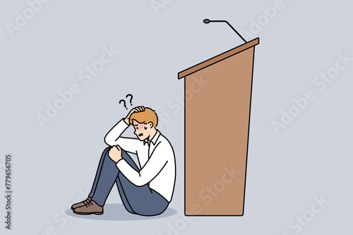 Man experiences peiraphobia, which causes fear speaking in front of audience, and sits near empty podium with microphone. Problem peiraphobia in person with no experience in conducting business events