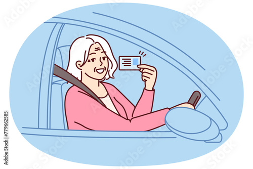 Happy elderly woman demonstrates driver license sitting behind wheel of car and rejoices at opportunity to go on road trip. Positive grey-haired old lady got driver ID after retirement © drawlab19