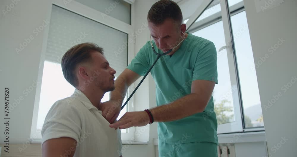 Middle-aged specialist using stethoscope checking young patient's breathing at the hospital room. Middle-aged specialist using stethoscope checking young patient's breathing at the hospital room.