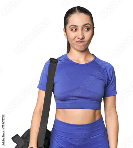 Athletic Caucasian young woman with gym bag on studio background confused, feels doubtful and unsure.