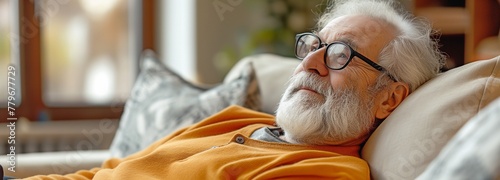 An optimistic and upbeat elderly man sitting on a sofa is seen from the side profile.