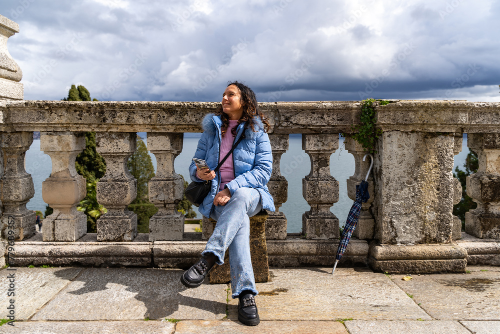 portrait of happy middle aged traveler woman on vacation sitting in an outdoor terrace in front of lake Maggiore
