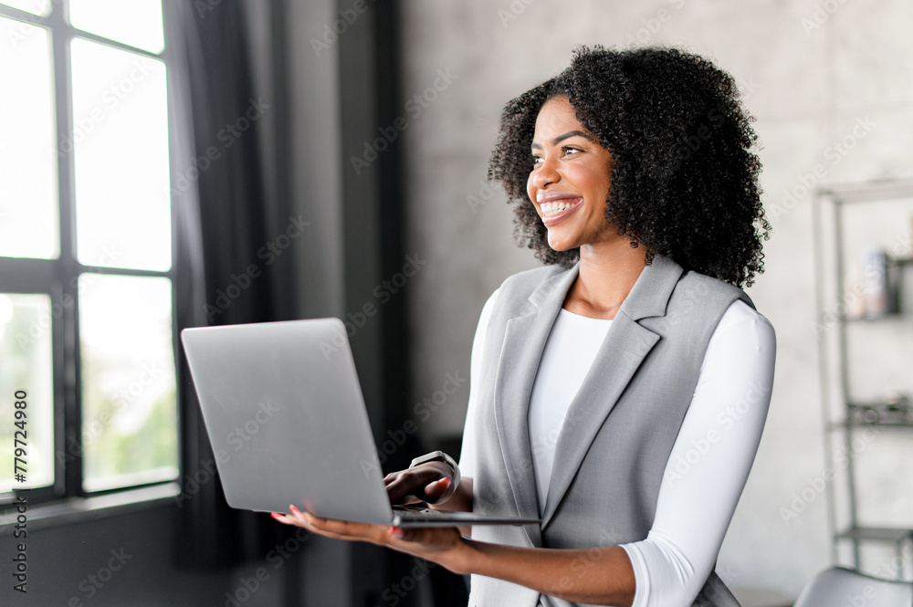 An upbeat African-American businesswoman engages with her computer, her smile suggesting a positive interaction or successful business venture. The blend of technology and business acumen An upbeat African-American businesswoman engages with her computer, her smile suggesting a positive interaction or successful business venture. The blend of technology and business acumen