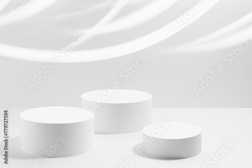 Set of three round white podiums for cosmetic products mockup, smooth glowing light lines on white background. Stage for presentation skin care products, gifts, goods, advertising in hipster style.