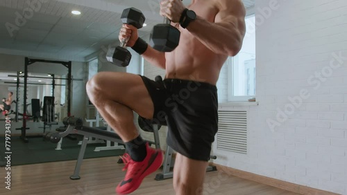 Young man is training in gym and running in place with dumbbells in his hands. Increases endurance and targets the deltoid muscles, biceps and shoulder girdle photo