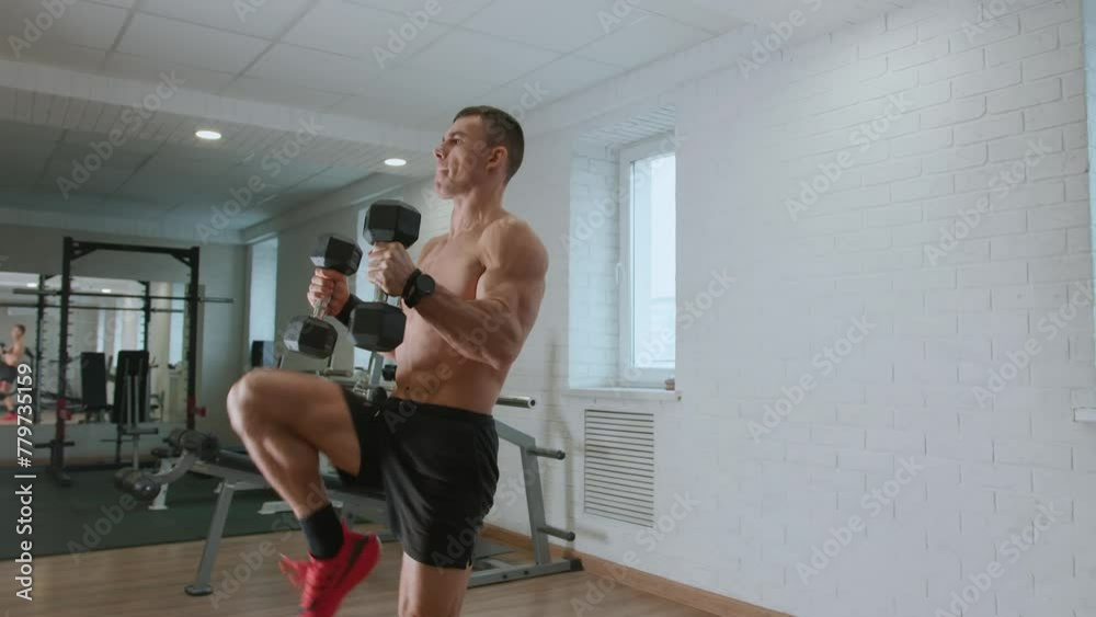 Young man is training in gym and running in place with dumbbells in his hands. Increases endurance and targets the deltoid muscles, biceps and shoulder girdle Young man is training in gym and running in place with dumbbells in his hands. Increases endurance and targets the deltoid muscles, biceps and shoulder girdle
