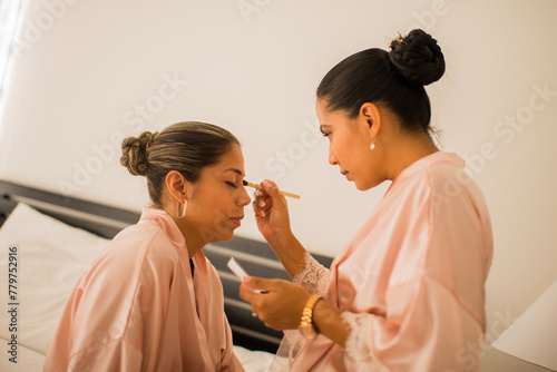 mujeres jovenes latinas frente a frente una de ellas ayudando a maquillar a su compañera  photo