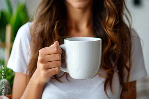 A woman gracefully holds an empty white mug, presenting it at the center, ideal for mockup purposes