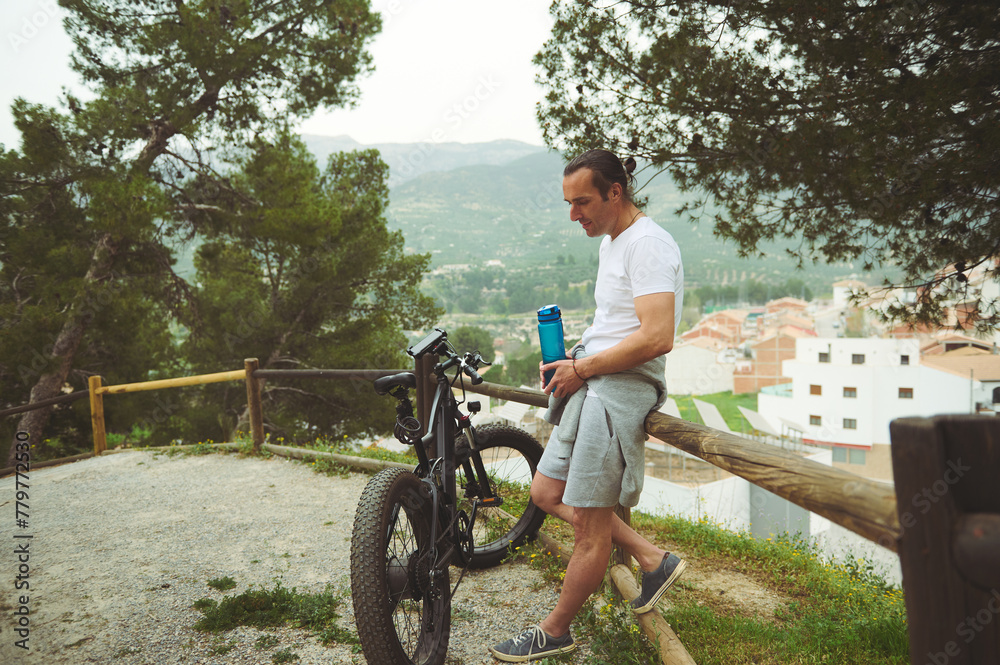 Cyclist, sportsman holding a bottle of water, having a break while riding using a motor-powered electric bicycle, a bike with pedal-assist system. Active people, nature and healthy lifestyle concept
