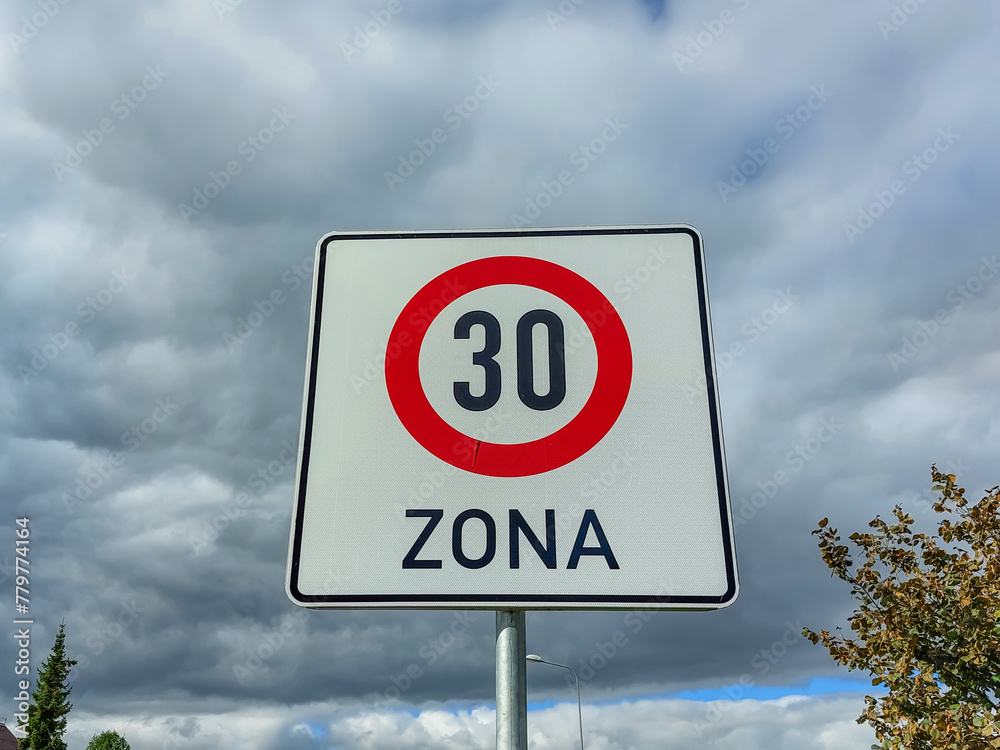 Metal road or traffic sign with number 30 in a red circle, and zone, indicating speed limit against blue sky and clouds background
