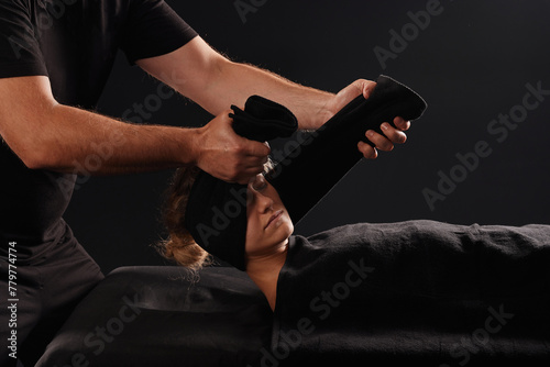 A professional massage therapist or massage therapist wraps a towel around a client's neck, performing a neck stretch. the client lies on the massage table covered with a towel
