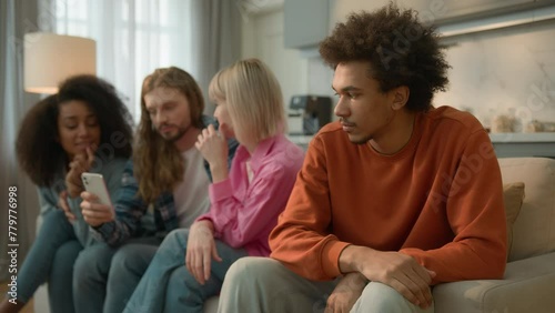 Separated sad frustrated stressed worried offended African American guy male introvert man migraine headache disinterest problem thinking ignoring multiracial friends talking friendly gossip at home