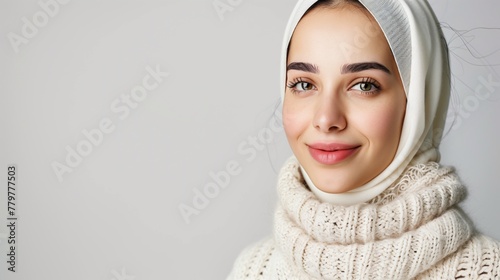Smiling young woman in white headscarf and knitted sweater, neutral background