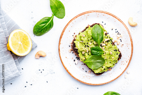 Avocado toasts with spinach and cashew nuts sprinkled with sesame seeds on white table background, top view