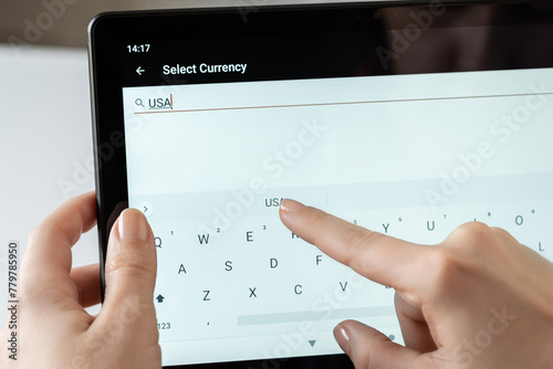 Woman finger of hand choosing foreign USA, dollar currency from the list on the tablet for buying choosing online shopping, searching booking hotel