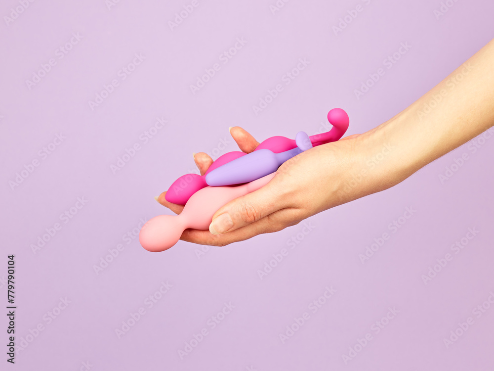 Fototapeta premium Woman's hand holding adult sex toys over violet background
