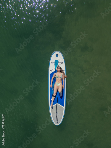 cenital vertical Young brunette Caucasian woman sunbathing on her surfboard in the middle of the sea