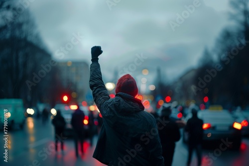 An activist demonstrating with a fist raised in protest amidst a blurred urban setting during a rain-soaked evening.