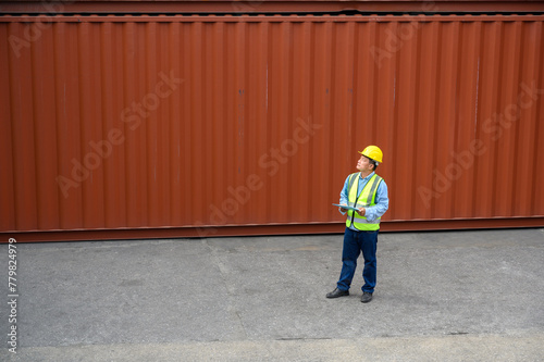 Foreman or Engineer wears yellow helmet and reflection shirt to control or check inventory details of containers box. Container loading cargo freight in import and export business logistic industry.