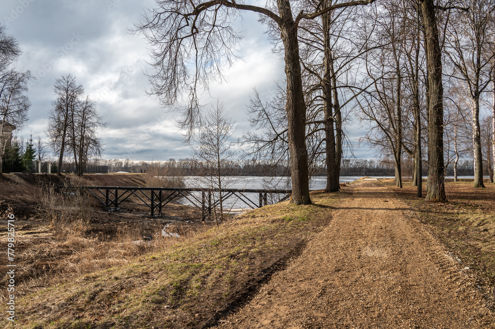 Fototapeta premium City park with alleys, walking paths and benches, a flowing river. Spring landscape.