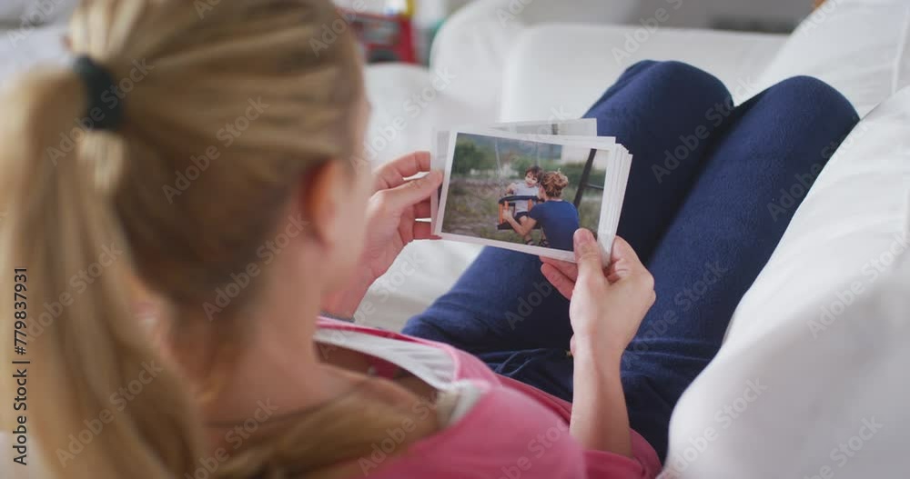Young mother lying on sofa in living room watching printed family photos Young mother lying on sofa in living room watching printed family photos