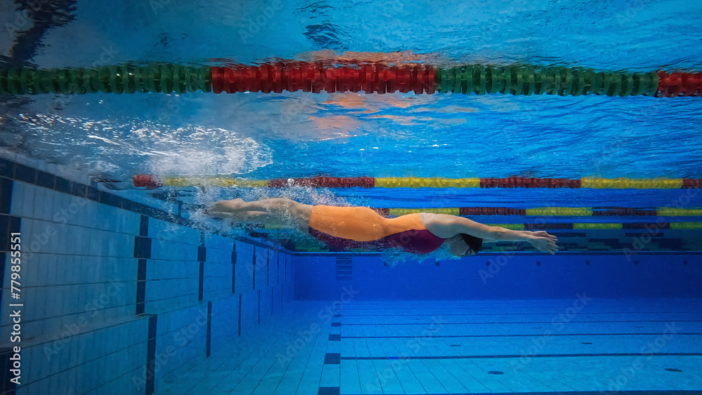 Female athlete swimming in the freestyle and making a flip turn to reverse direction in the pool, underwater wide. - obrazy, fototapety, plakaty 