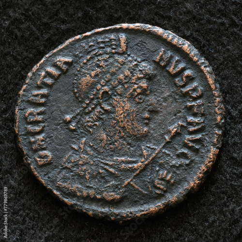 Ancient Roman coin of Emperor Gratian, top view of vintage metal money isolated on black background. Concept of old texture, Rome, portrait, Empire, antique and history