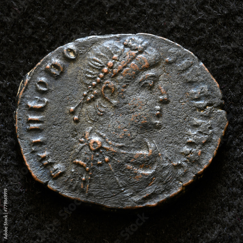 Ancient Roman coin of Emperor Theodosius I the Great, top view of vintage metal money isolated on black background. Concept of old copper texture, Rome, Byzantine Empire, antique